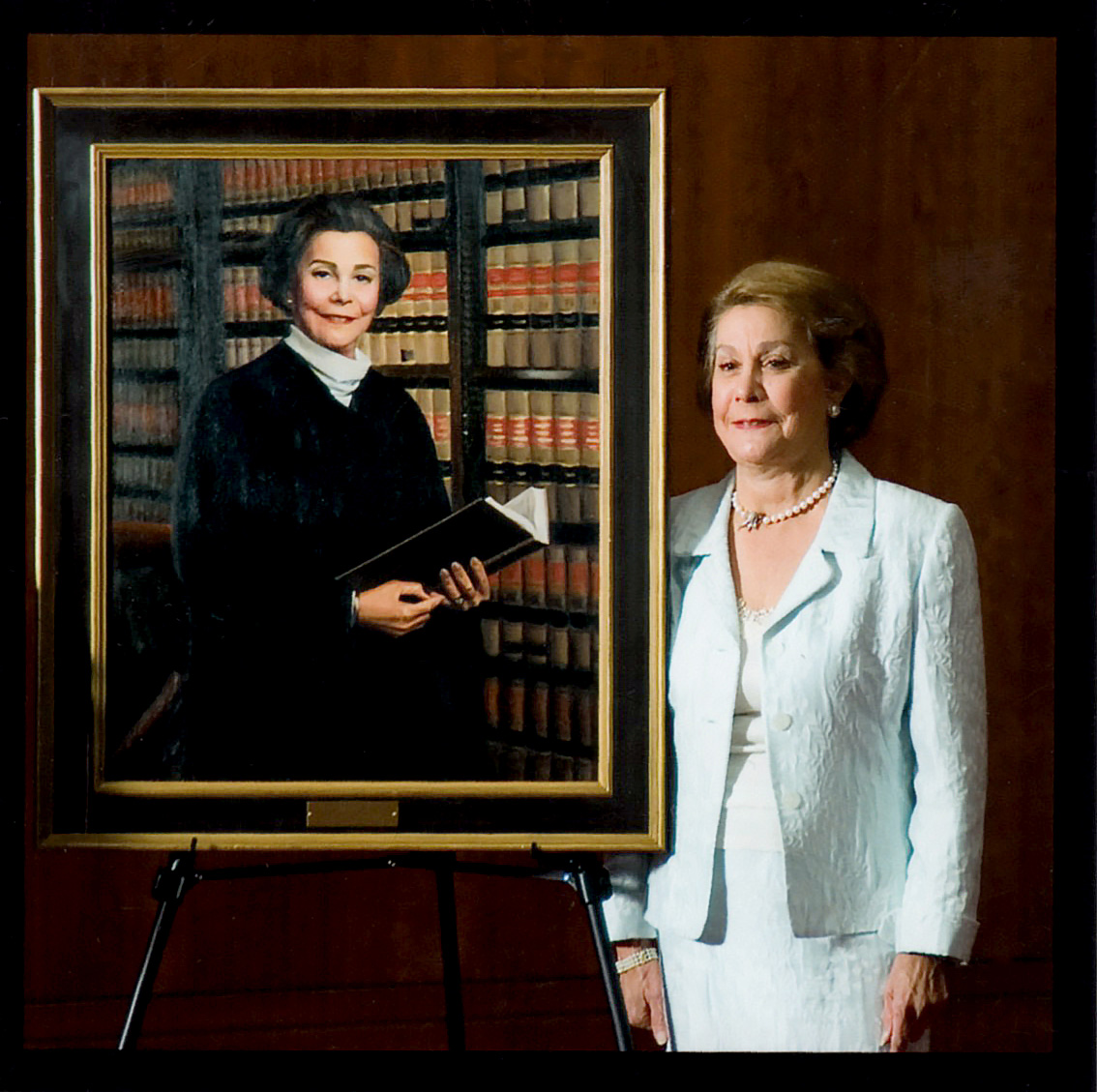 Justice Ruby Kless Sondock standing beside a framed judicial portrait in a formal setting